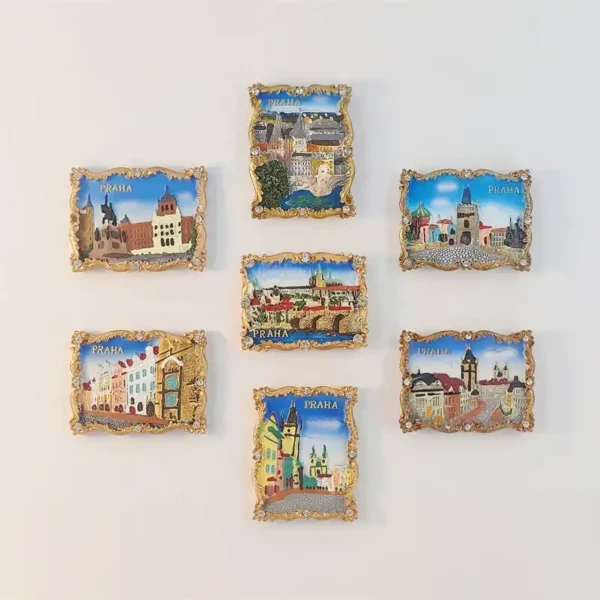 Seven Prague scene fridge magnets with ornate gold-tone borders, clear faceted accents and PRAHA lettering, arranged on a light background.